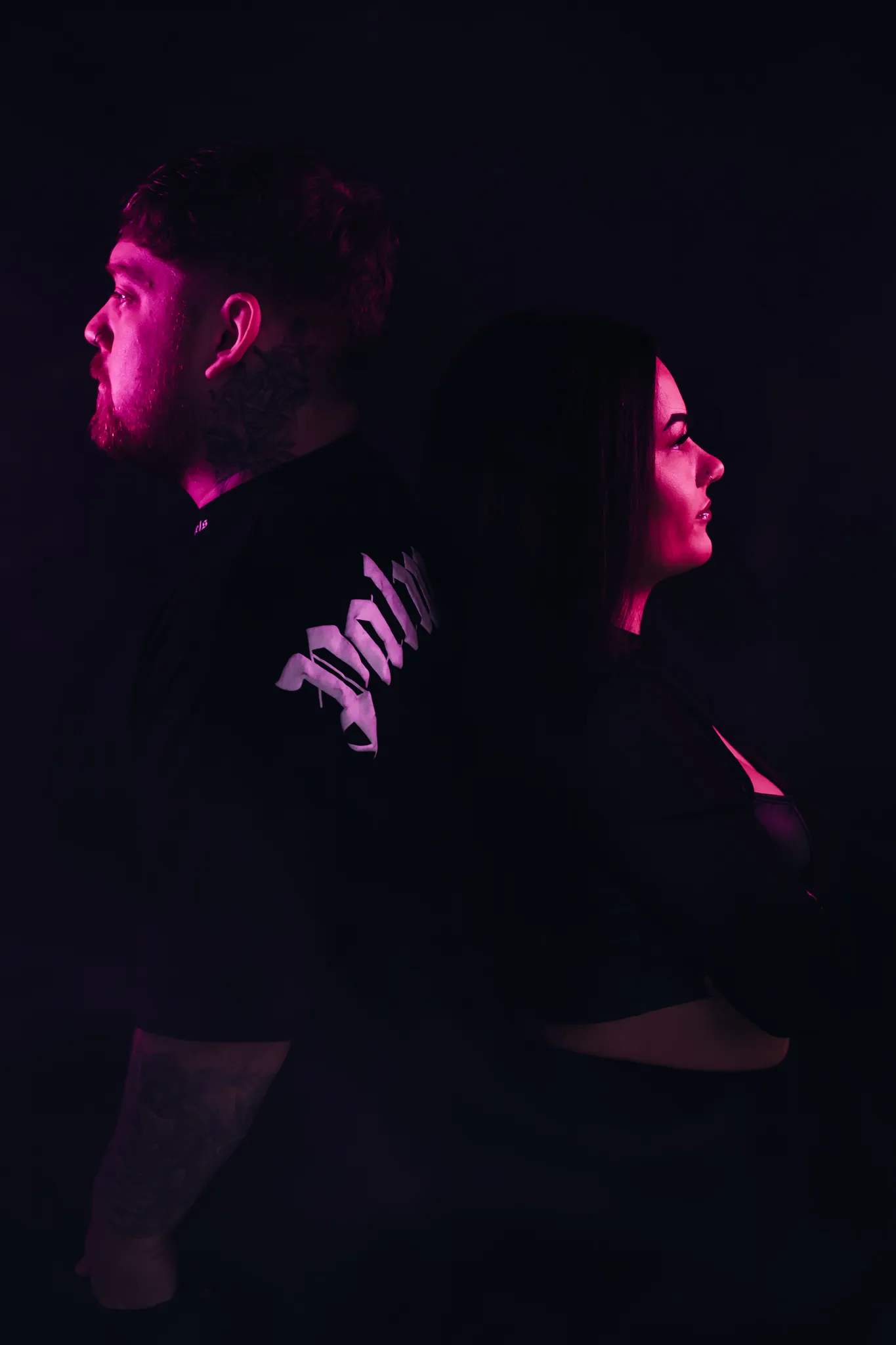 Jamie McLucas and Britney Haynes standing back to back under magenta light